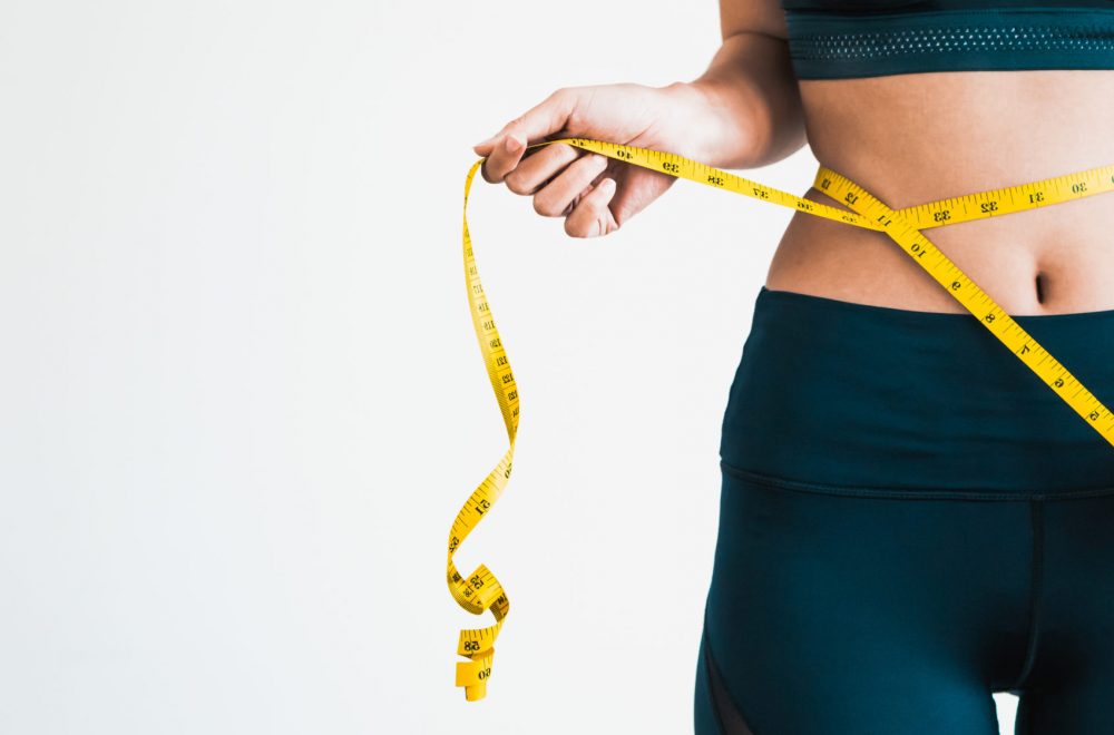 Close up shot of woman with slim body measuring her waistline and torso. Healthy nutrition and weight losing concept.